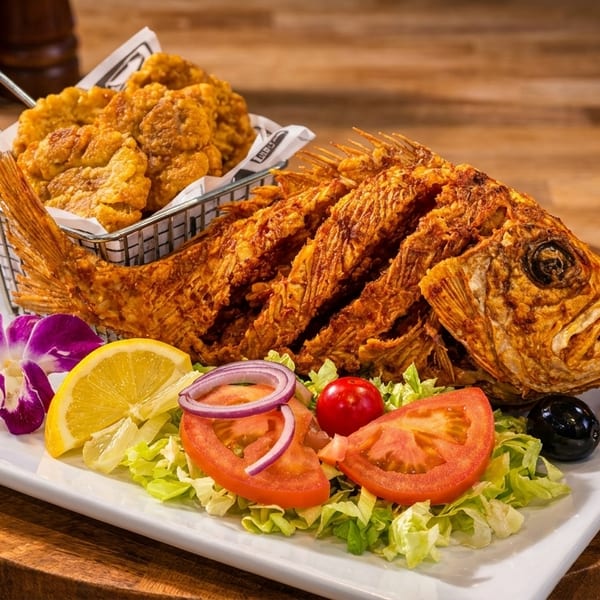 Crispy whole fried fish with a side of fried plantains, salad, lemon, and a purple orchid.
