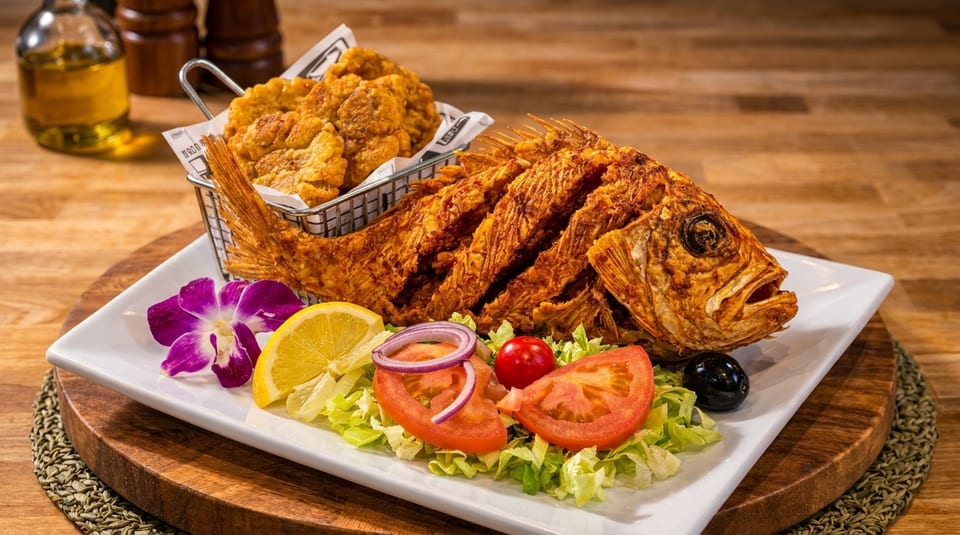 Crispy whole fried fish with a side of fried plantains, salad, lemon, and a purple orchid.