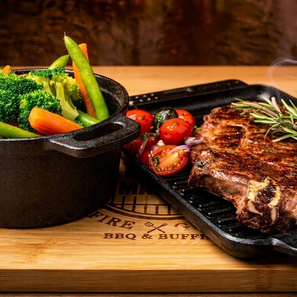 Steaming grilled steak with rosemary, roasted vegetables, and tomatoes on a wooden board.