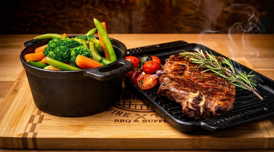 Steaming grilled steak with rosemary, roasted vegetables, and tomatoes on a wooden board.
